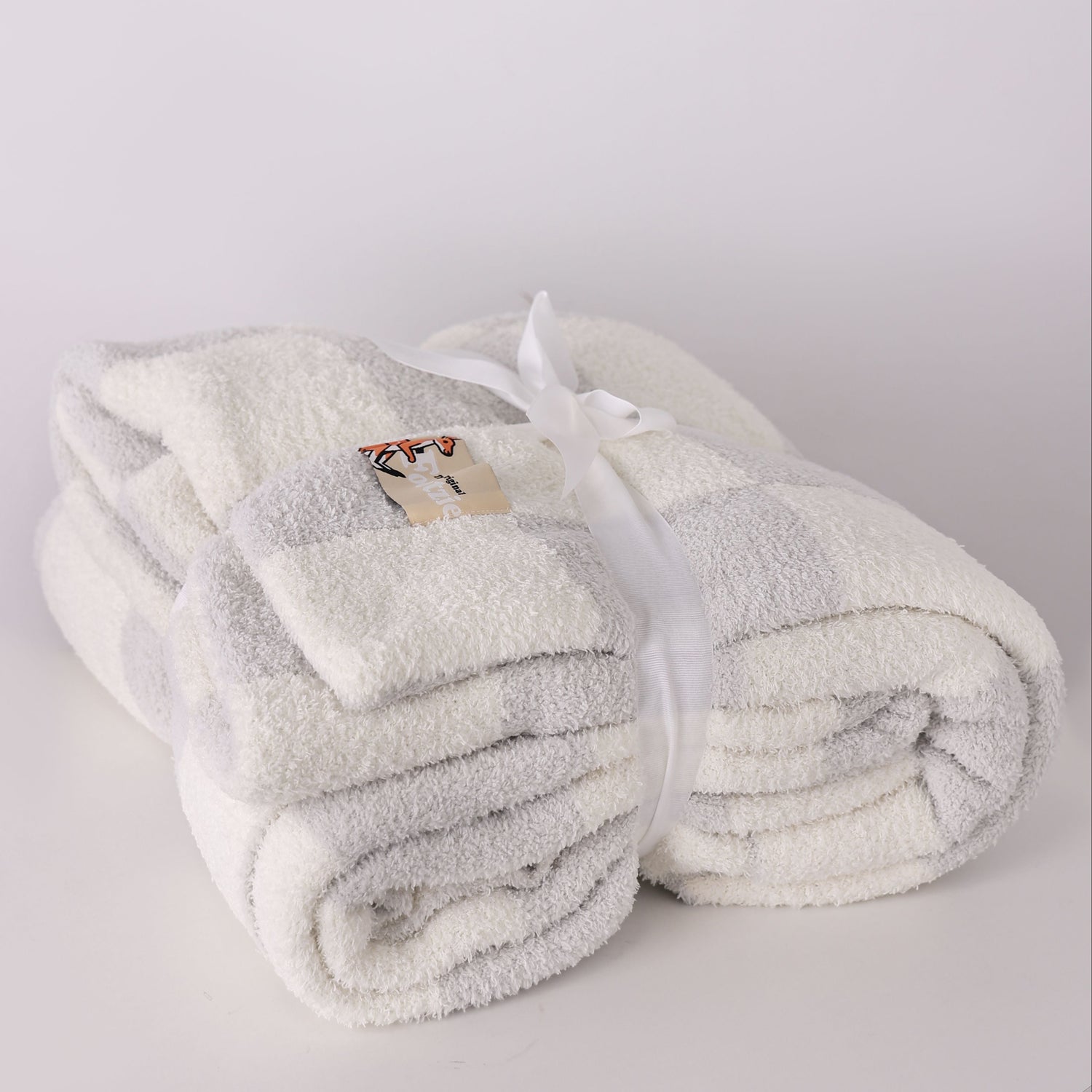 Folded white and grey blanket with a brand label on a light gray background