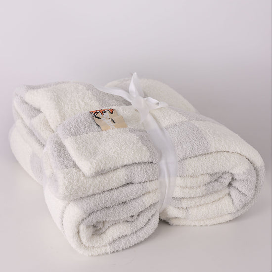 Folded white and grey blanket with a brand label on a light gray background