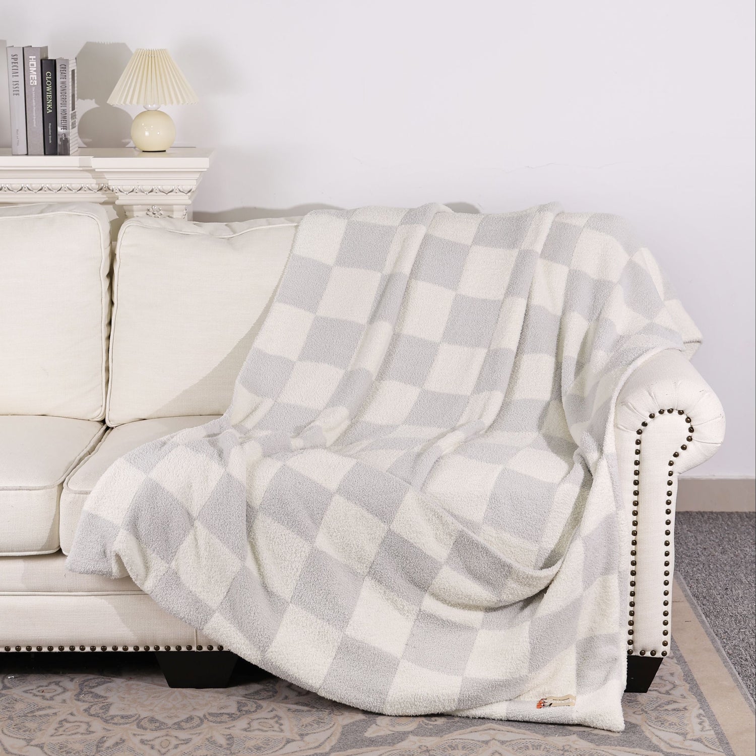 Gray checkered blanket draped over a white sofa against a white wall.